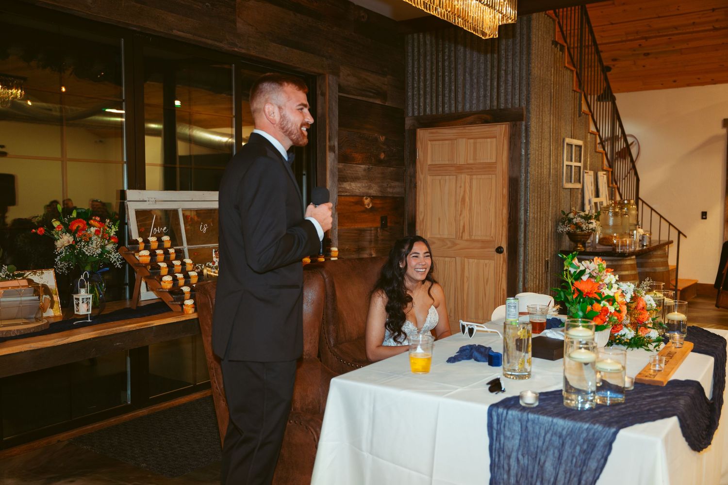 Wedding celebration in a rustic barn venue with exposed wooden beams and elegant table settings.