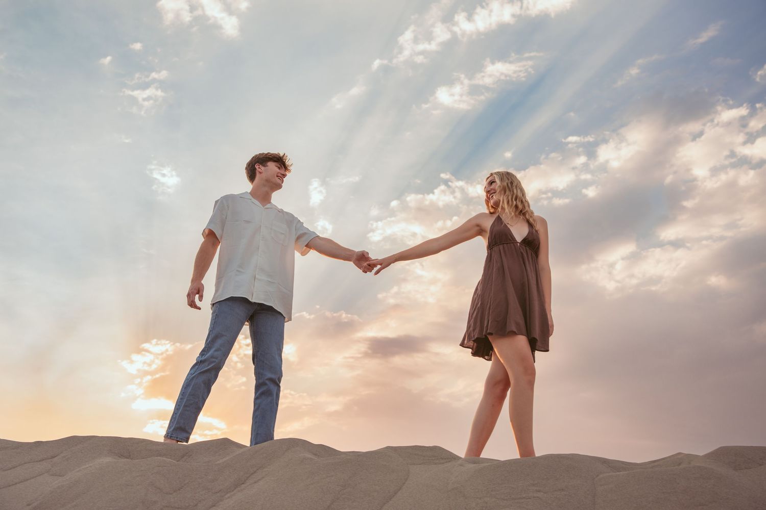 Silhouettes of couple holding hands while walking along desert sand dunes at dusk.