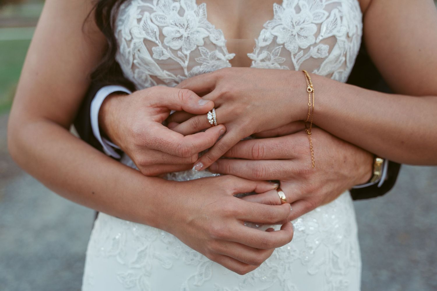 Close-up of hands with wedding rings and lace dress details.