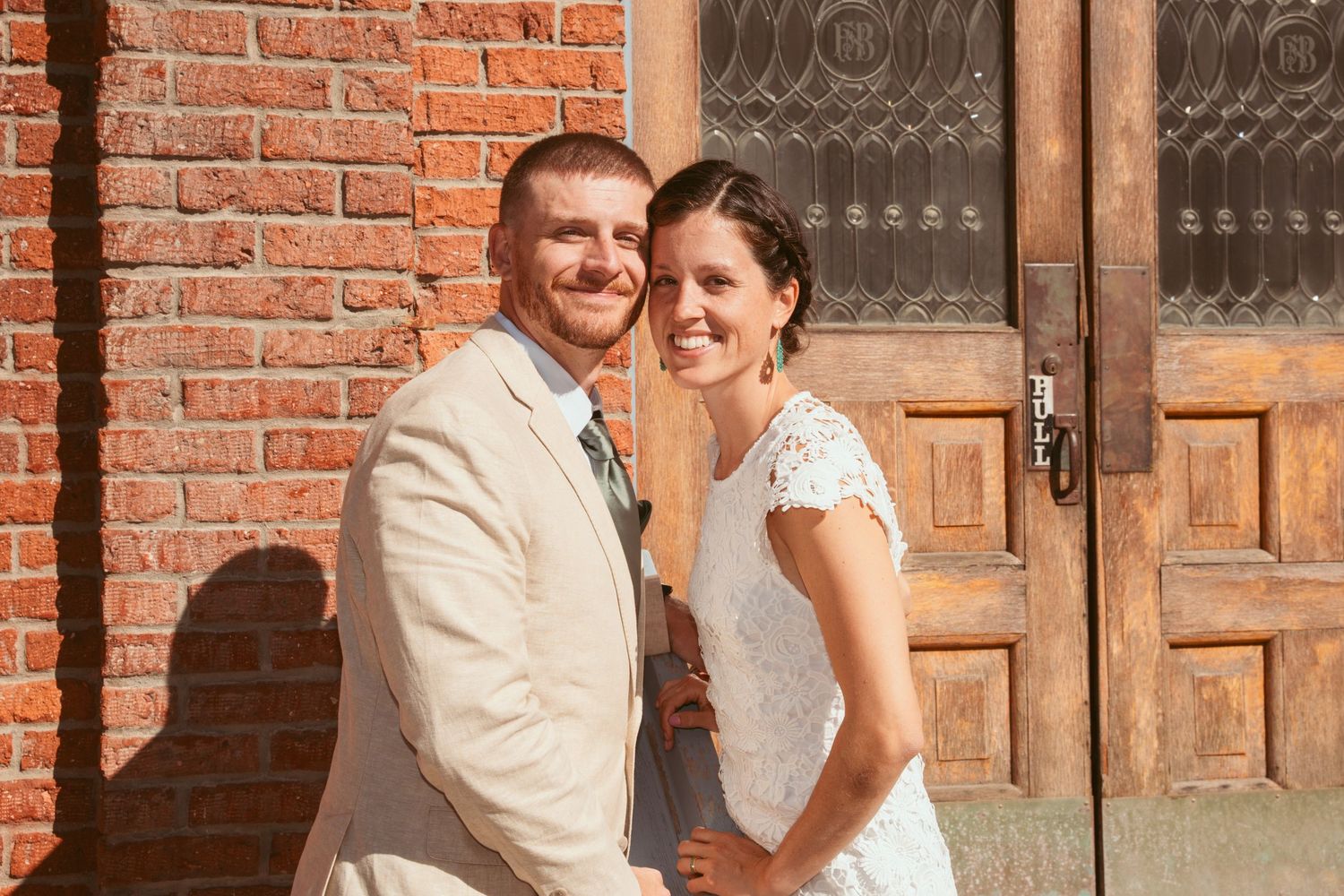 A couple shares a romantic moment against a rustic brick wall during their wedding.