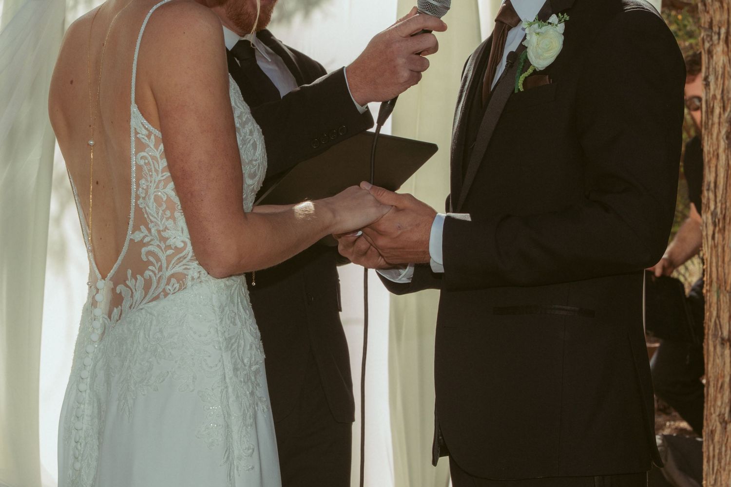 Close-up of wedding ceremony vows being exchanged in front of white curtains and trees.