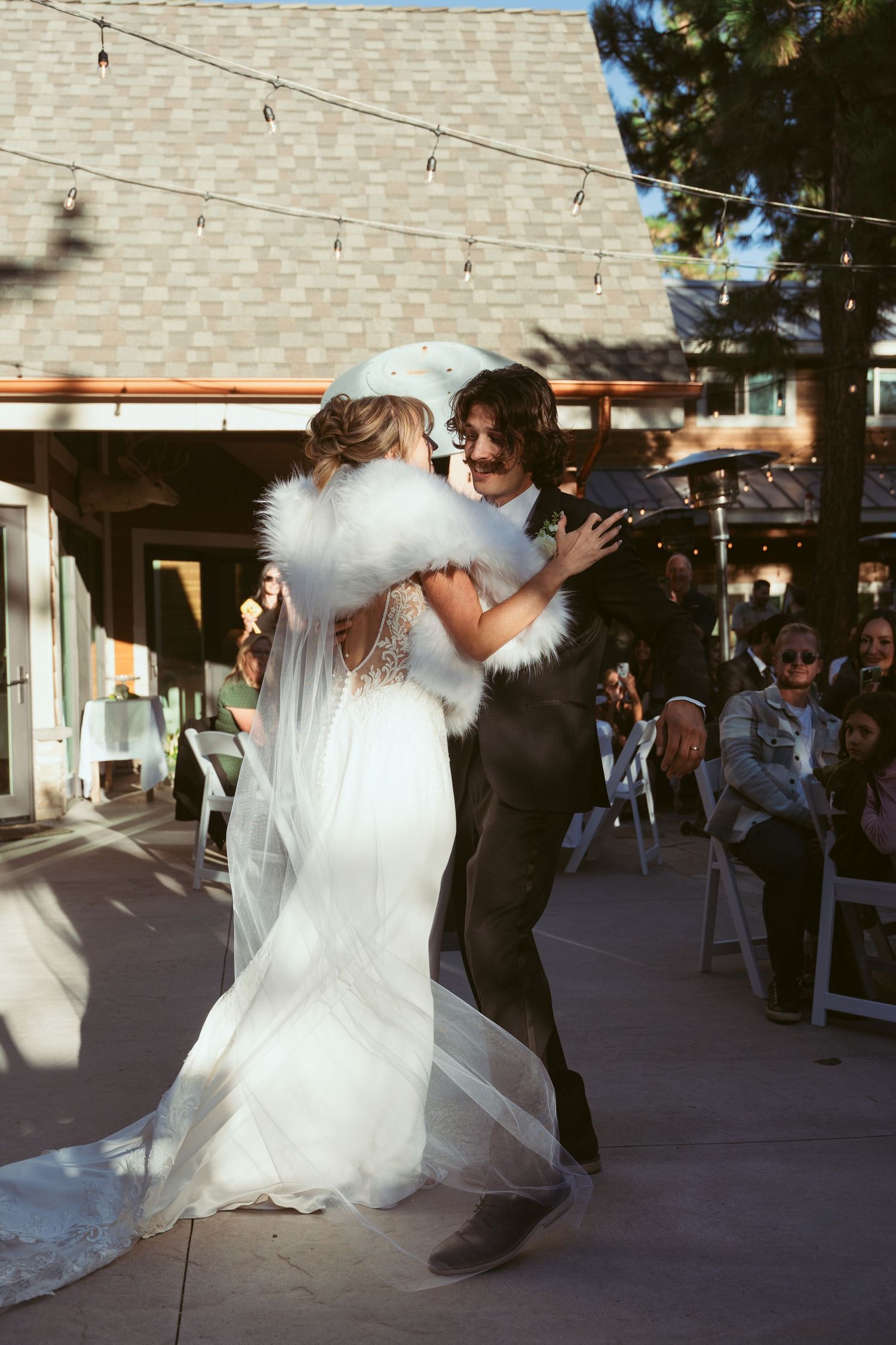 A couple dances beneath string lights at their outdoor wedding reception.