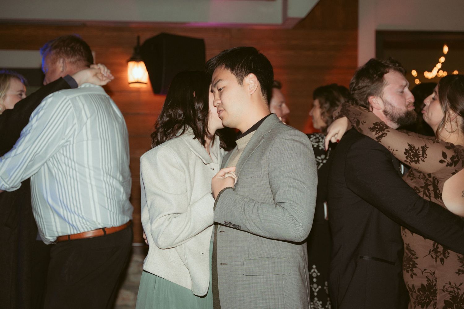 Couples slow dancing together at an evening reception with ambient lighting.