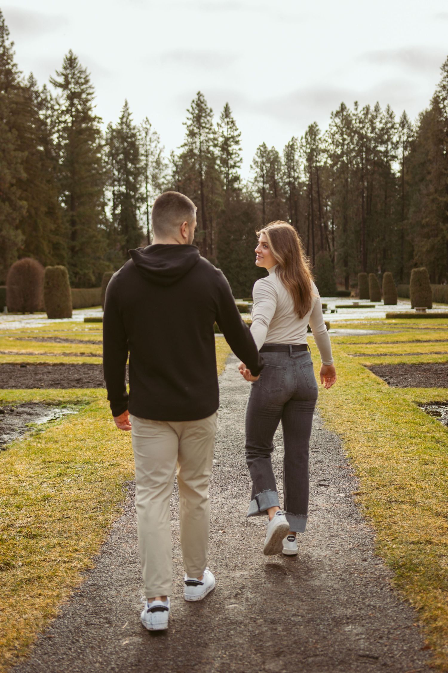 Back view of couple strolling together on a dirt path with pine trees in the background.