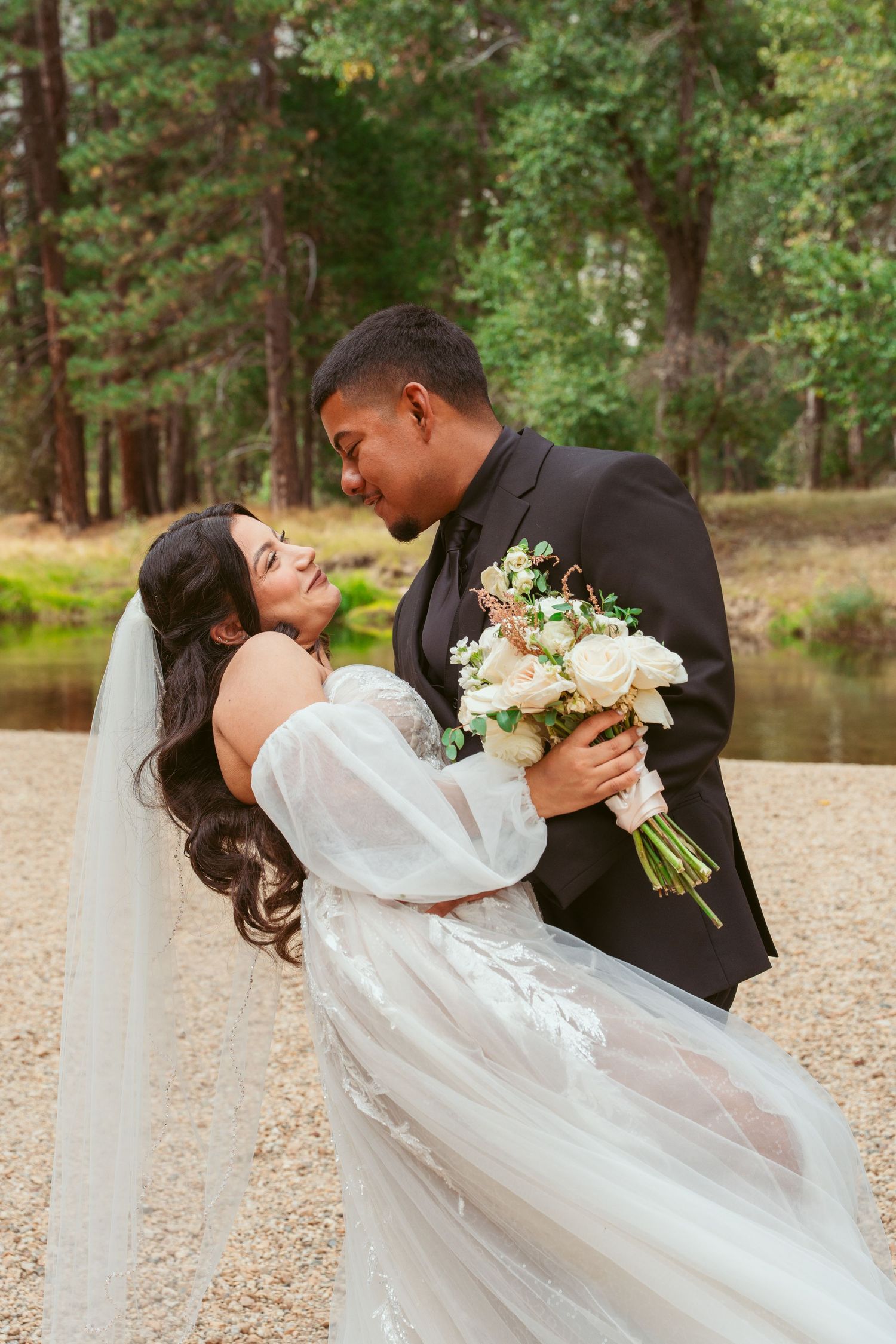 Romantic wedding couple sharing an intimate dip kiss while holding a white floral bouquet.