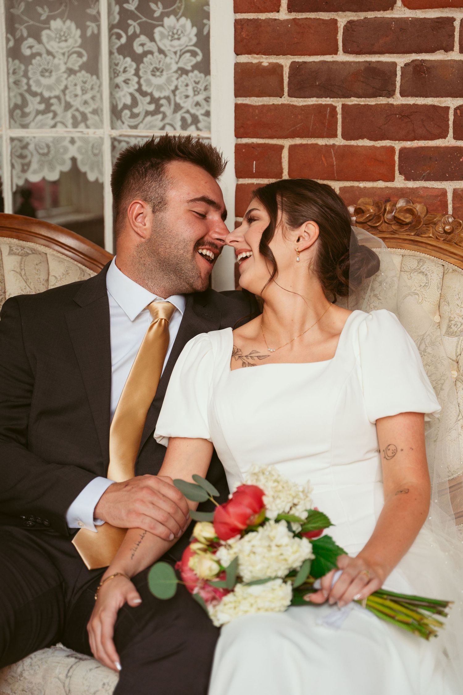 A candid moment of laughter between newlyweds seated on an antique sofa.