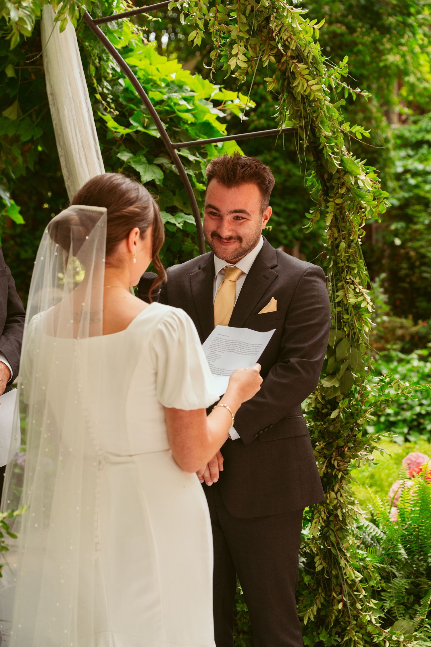Wedding couple sharing tender moment during garden ceremony under white fabric draping.