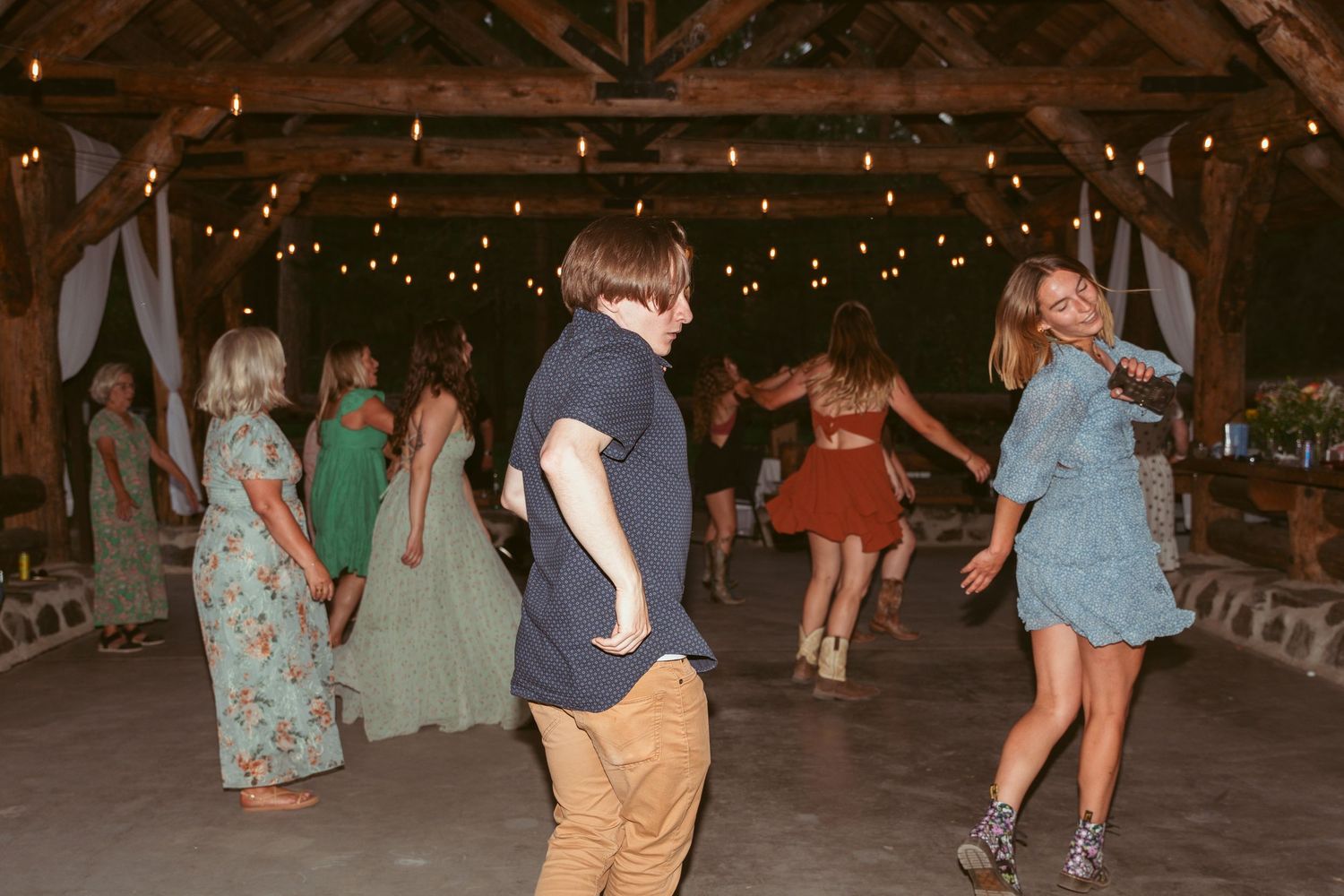 Guests dancing at a rustic venue with exposed wooden beams and string lights.