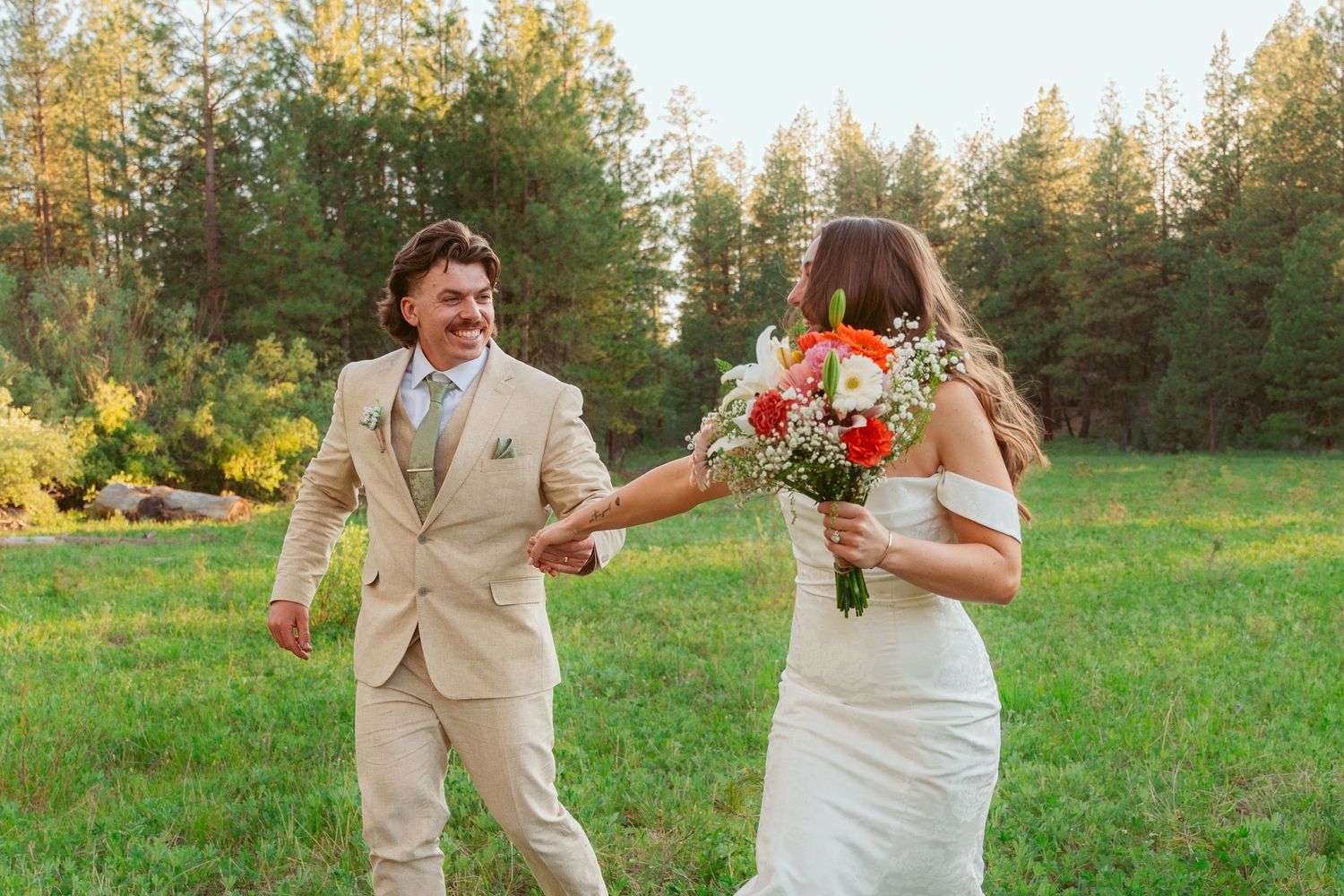 Newlyweds celebrate with playful movements in an outdoor field during sunset.