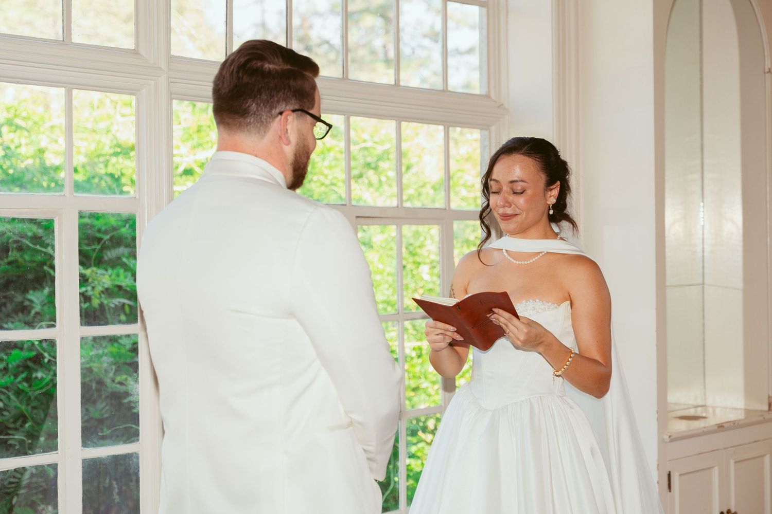 Elegant white wedding ceremony space with large windows and natural light streaming in.