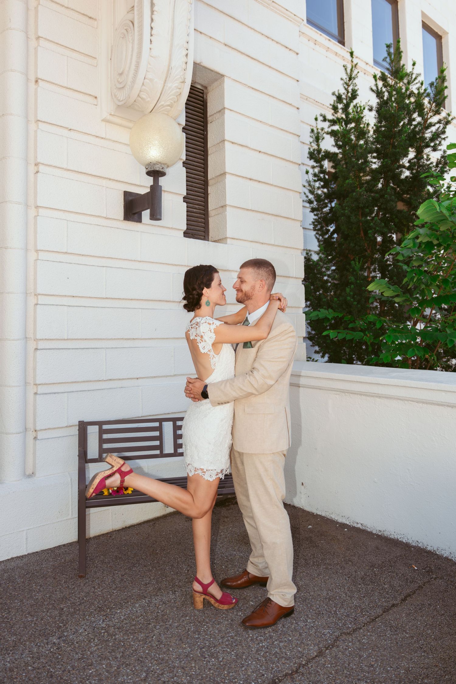 A couple shares a playful moment on a white building exterior during their first look.