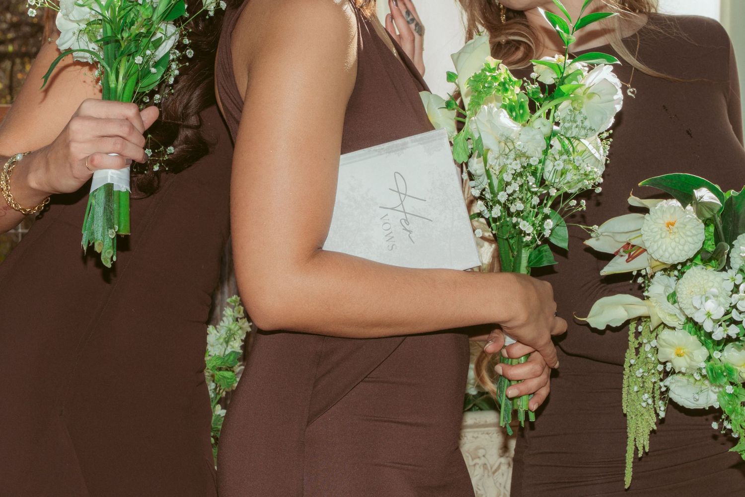 Close-up of brown bridesmaid dresses and white floral bouquets at outdoor wedding.