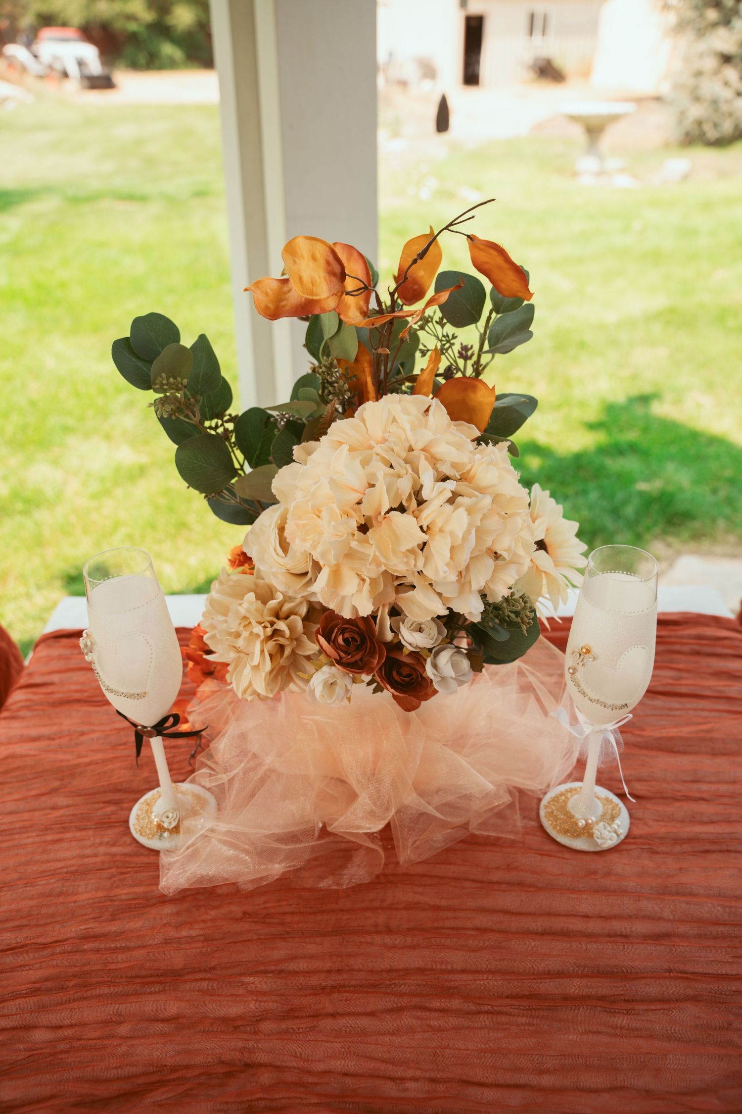Elegant table setting with white floral centerpieces and eucalyptus leaves on a burgundy tablecloth.