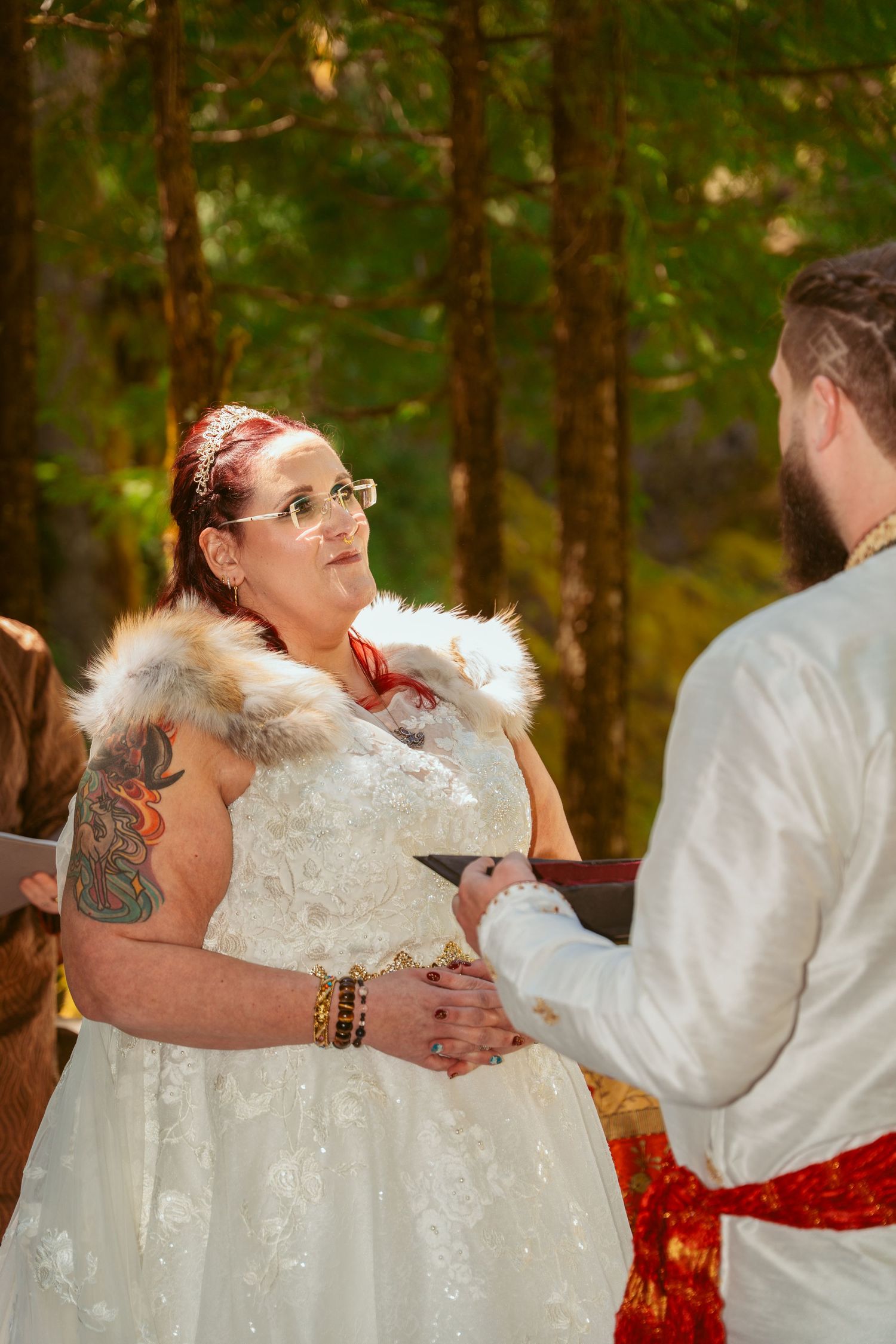 A romantic wedding ceremony moment with a couple in white attire embracing against a forest backdrop.
