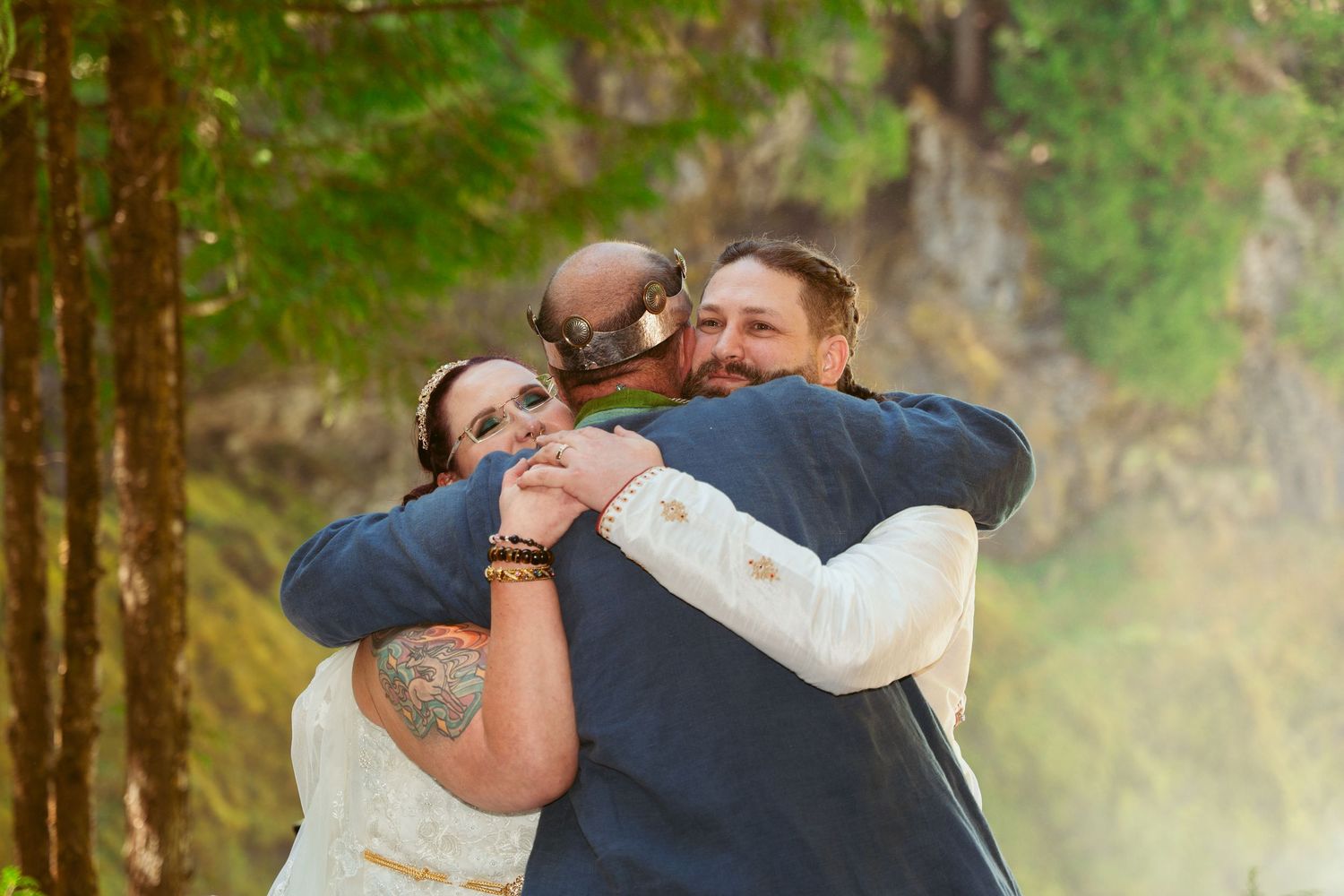 A heartfelt group hug during an outdoor wedding ceremony in a forest setting.