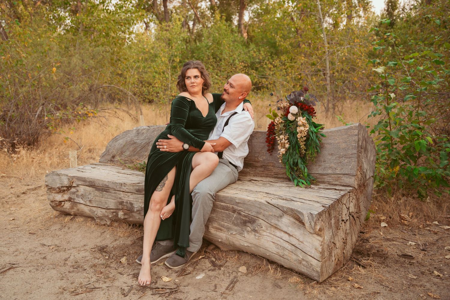 Romantic couple poses together on a fallen tree trunk in an autumn outdoor setting.