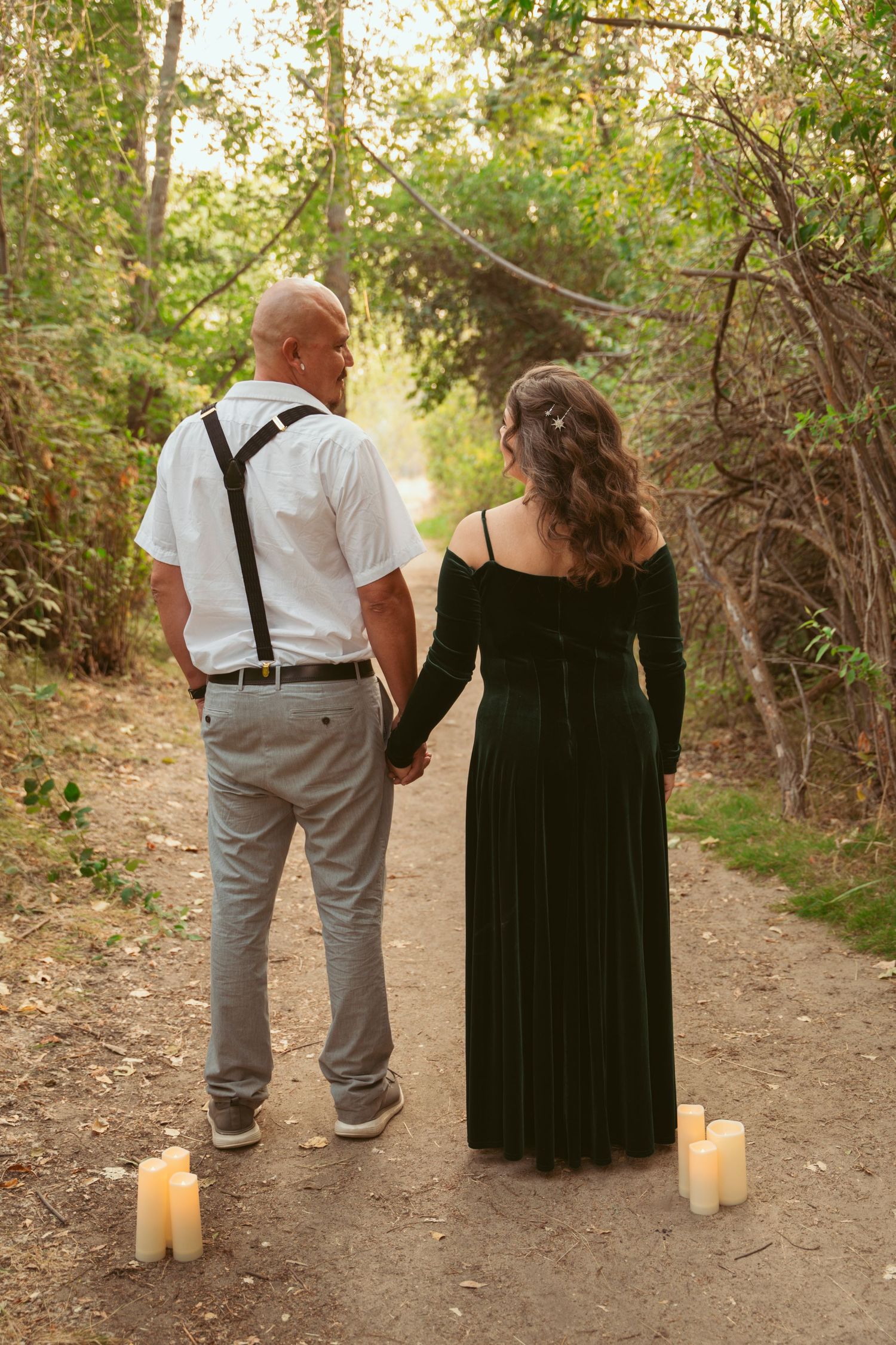 A couple walking on a dirt path with lit candles creating a romantic ambiance at dusk.