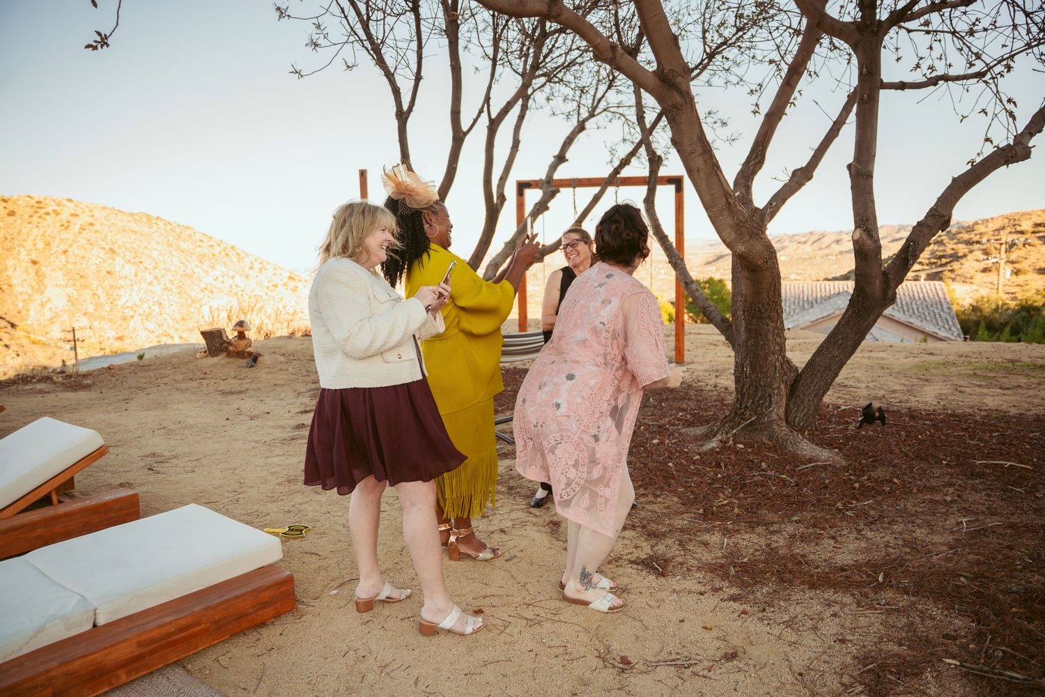 Wedding party gathering under trees during sunset desert ceremony.
