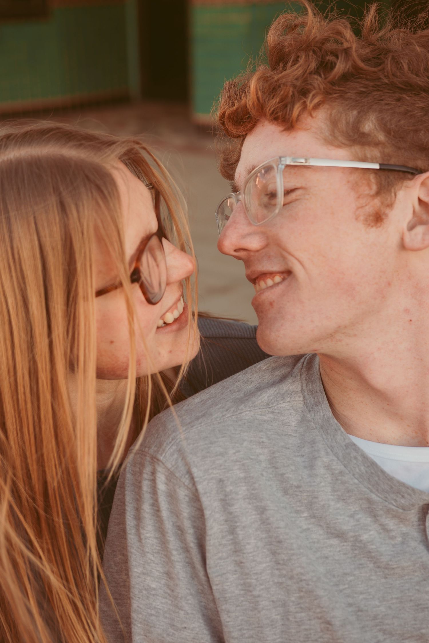 A couple in glasses sharing an intimate moment while smiling at each other indoors.