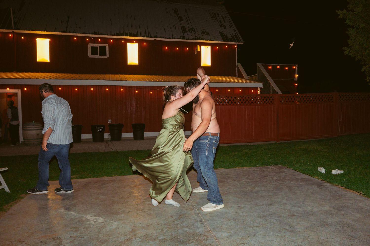 Evening outdoor wedding reception with string lights and red barn in background.