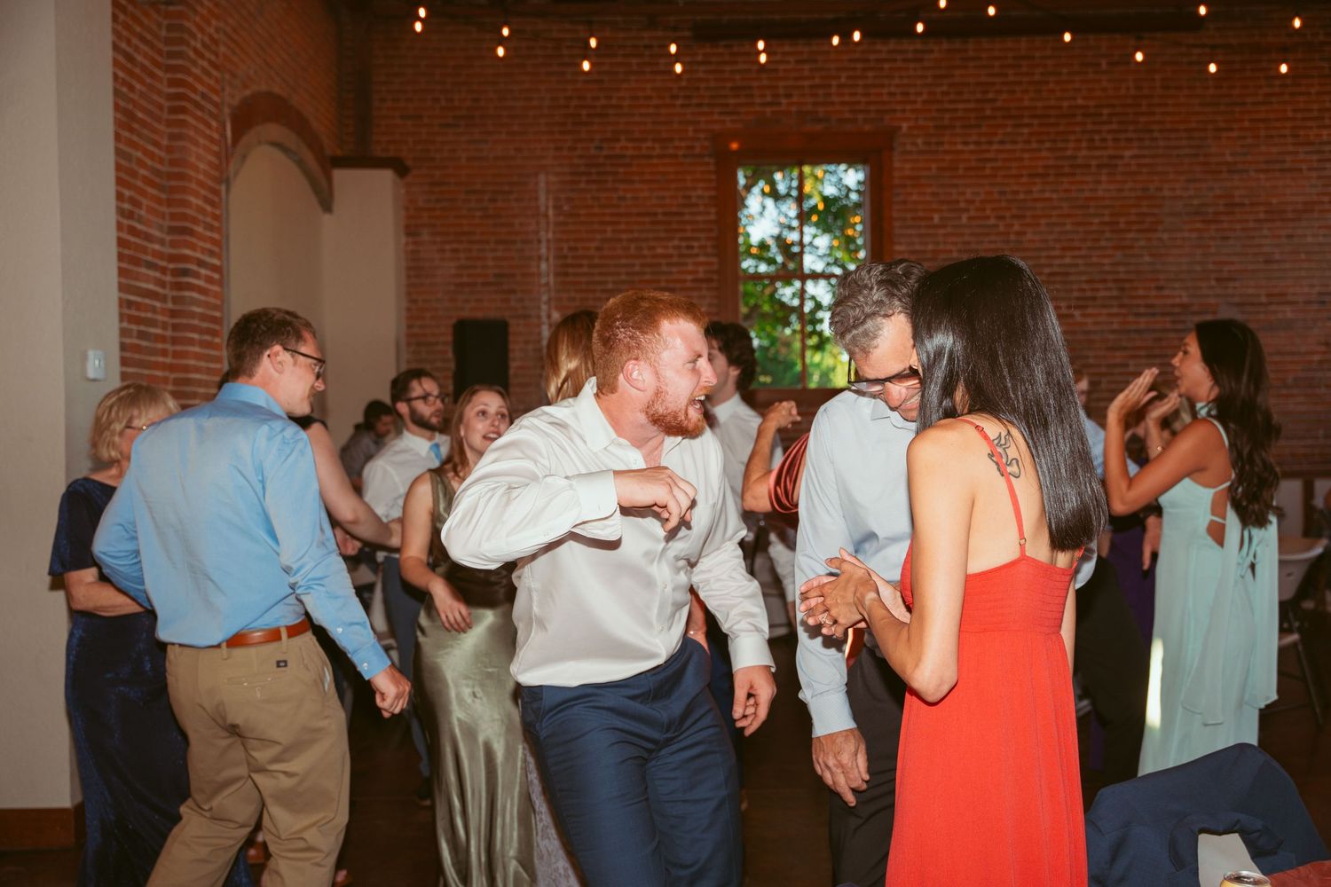 Wedding reception dance floor filled with guests enjoying themselves under string lights.