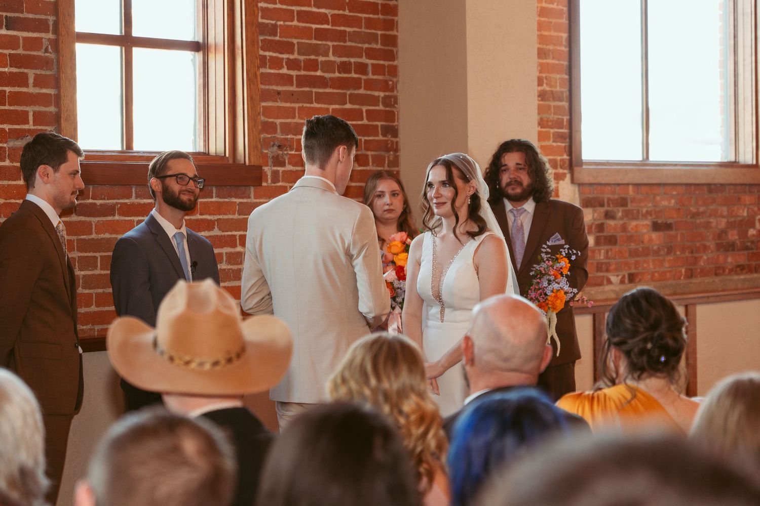 Wedding guests seated in rows during ceremony in brick-walled venue with natural light.