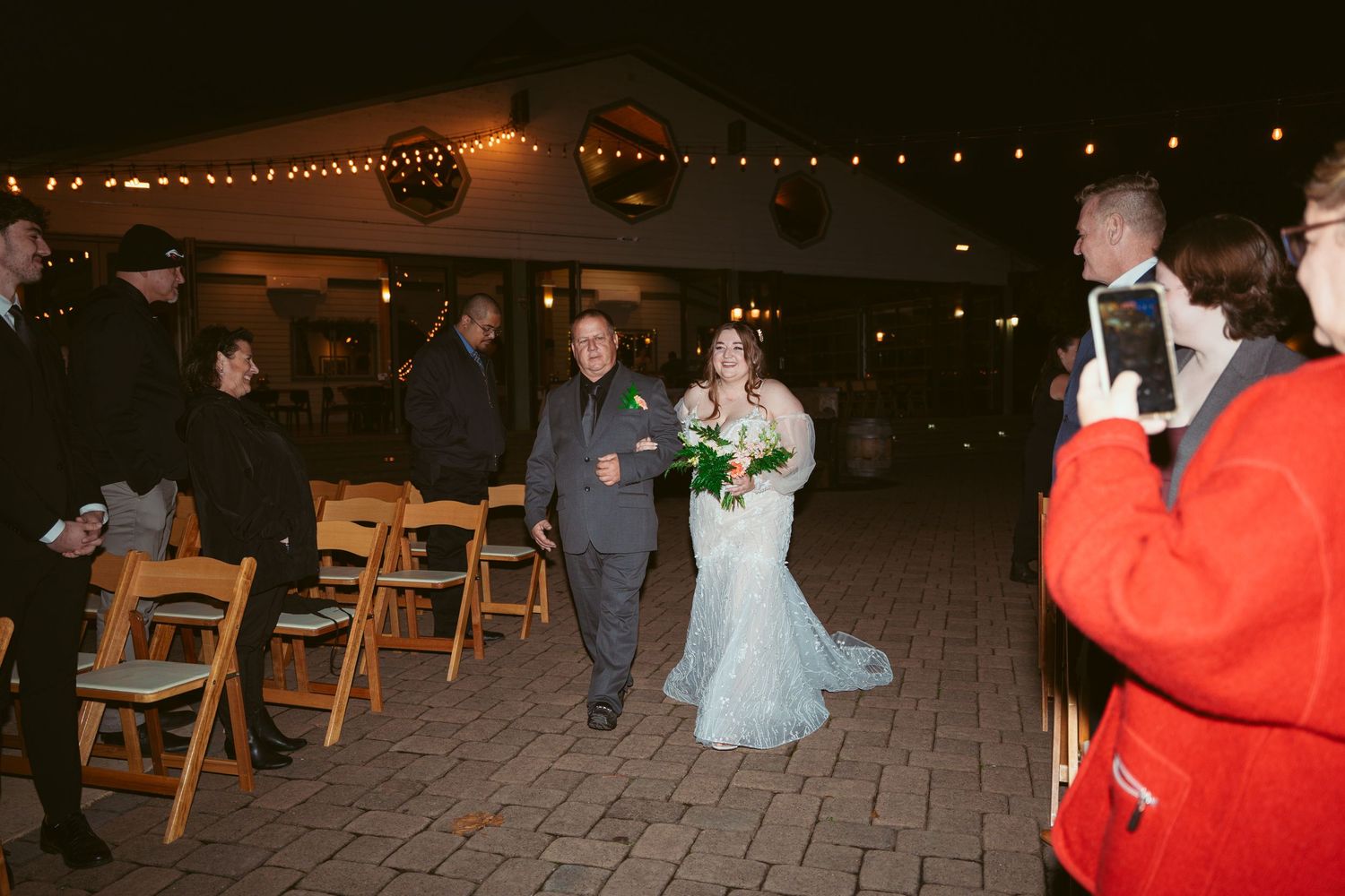Evening outdoor wedding reception with guests and string lights overhead.