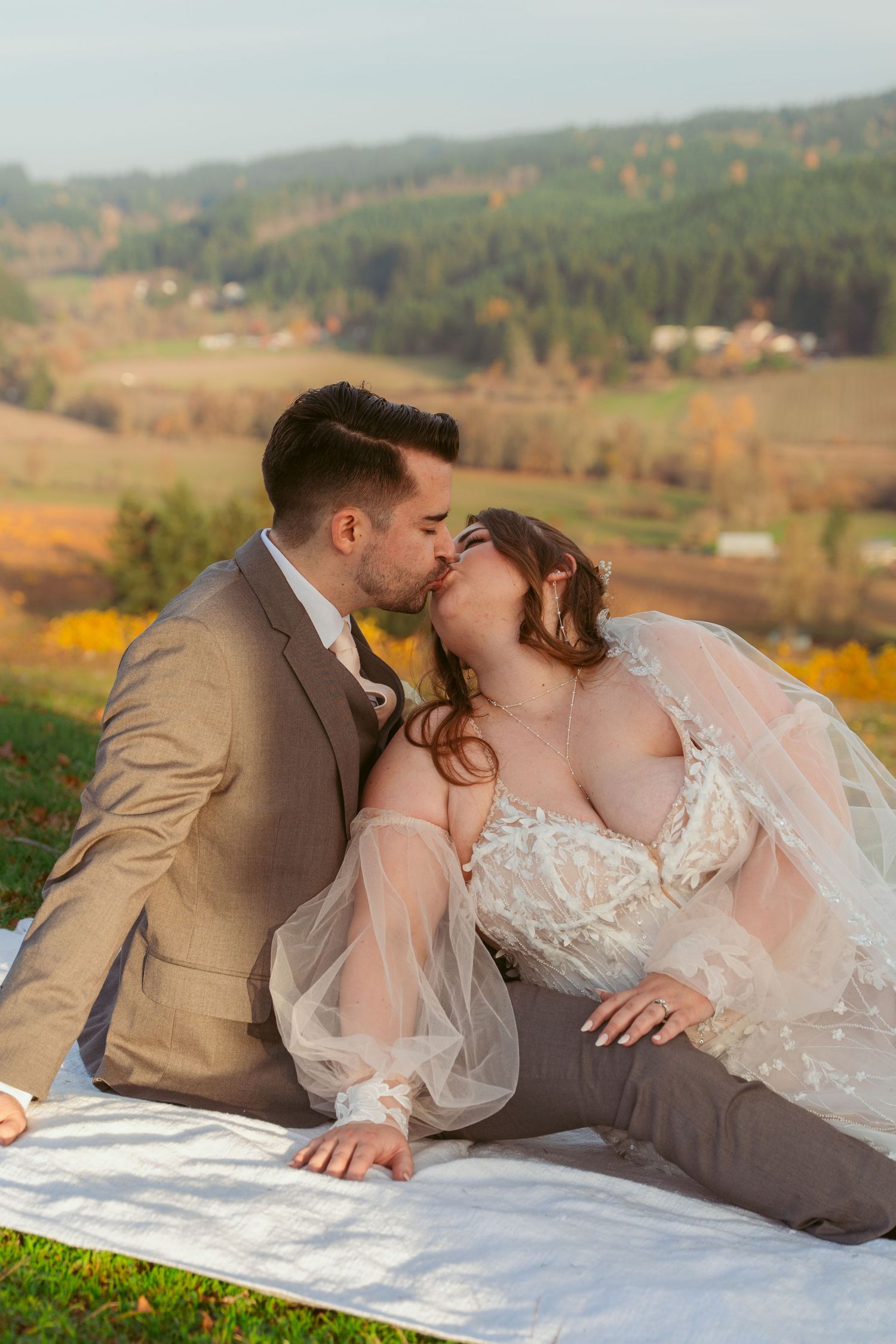 Intimate wedding photo of couple laying on white blanket with mountain vista.