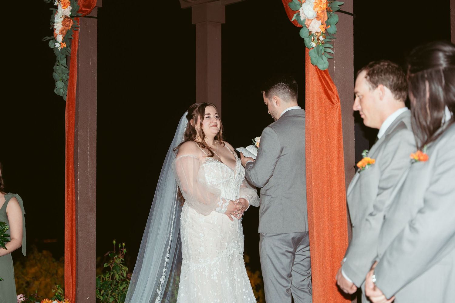 Couple exchanging vows during outdoor nighttime ceremony under decorated pavilion.