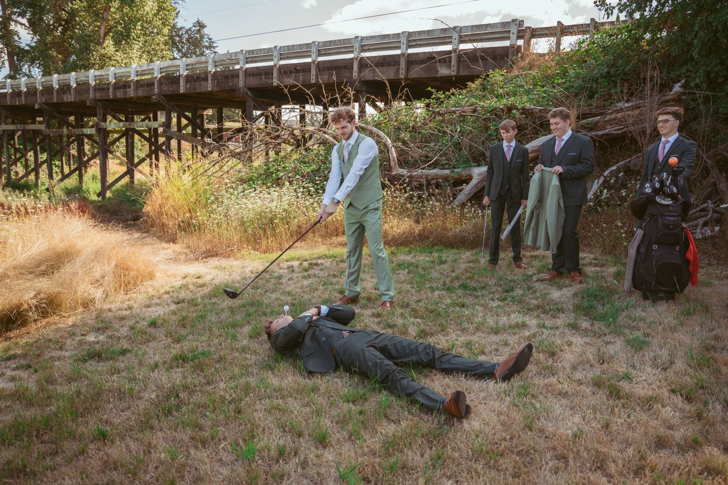 Wedding party members pose dramatically on ground for creative outdoor photo sequence.