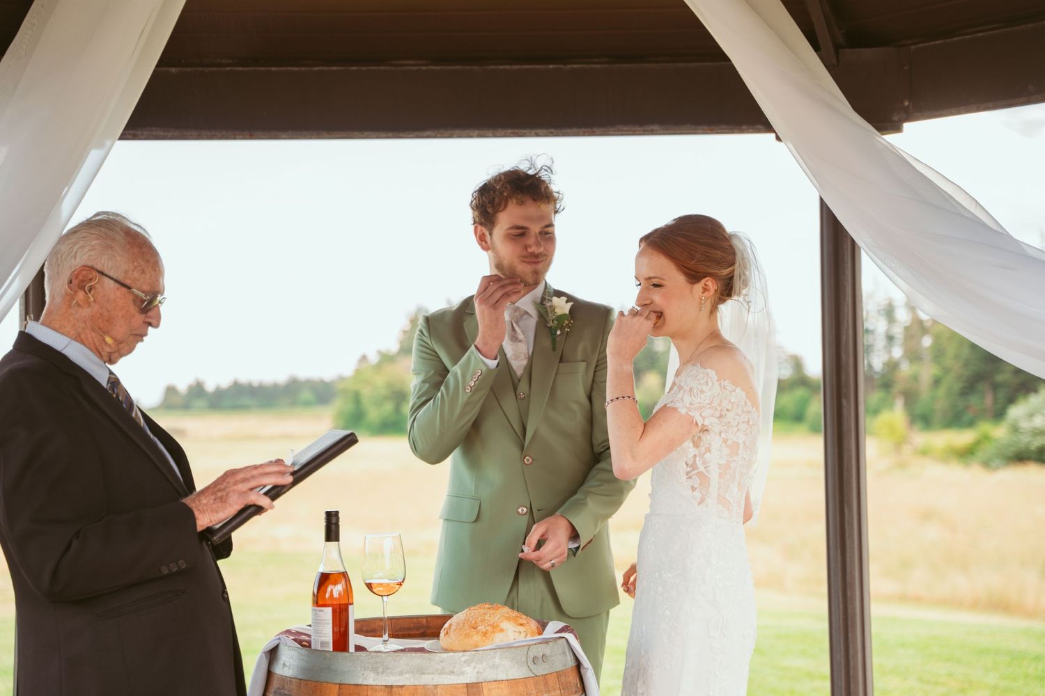 Wedding ceremony scene under covered pavilion with white draping and wooden beams.