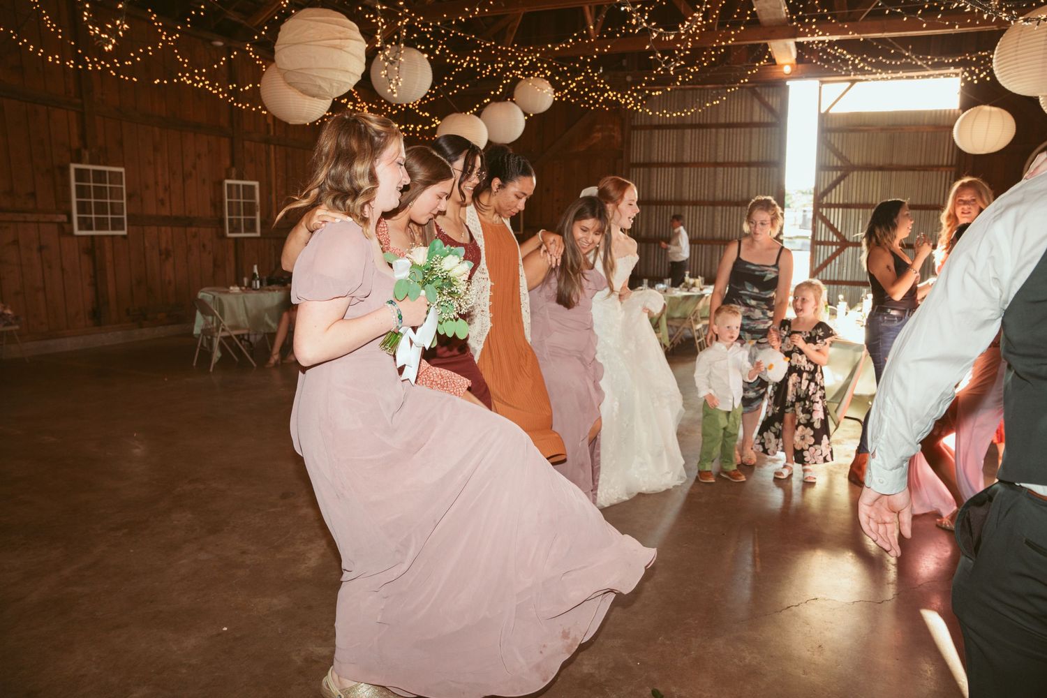Wedding celebration features lively dancing under decorative paper lanterns in a rustic barn venue.