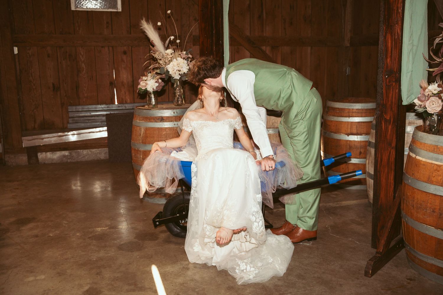 Wedding party members dancing and celebrating near wooden barrels in a rustic setting.