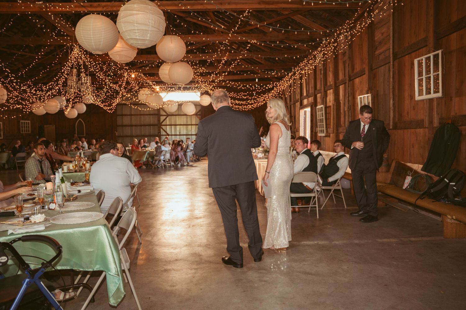 Wedding reception in rustic barn venue decorated with string lights and paper lanterns.