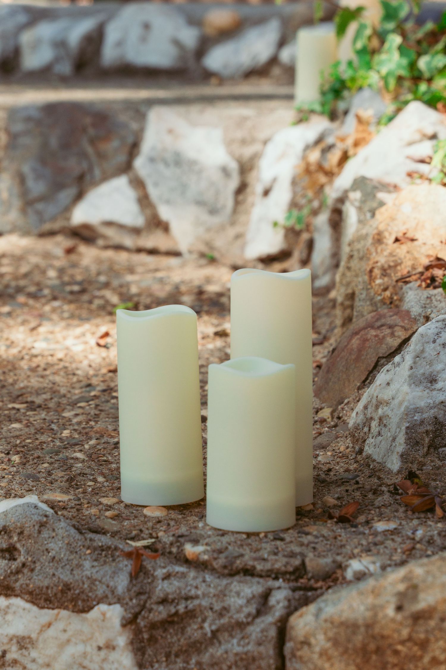 White pillar candles arranged on rustic stone steps in an outdoor setting.