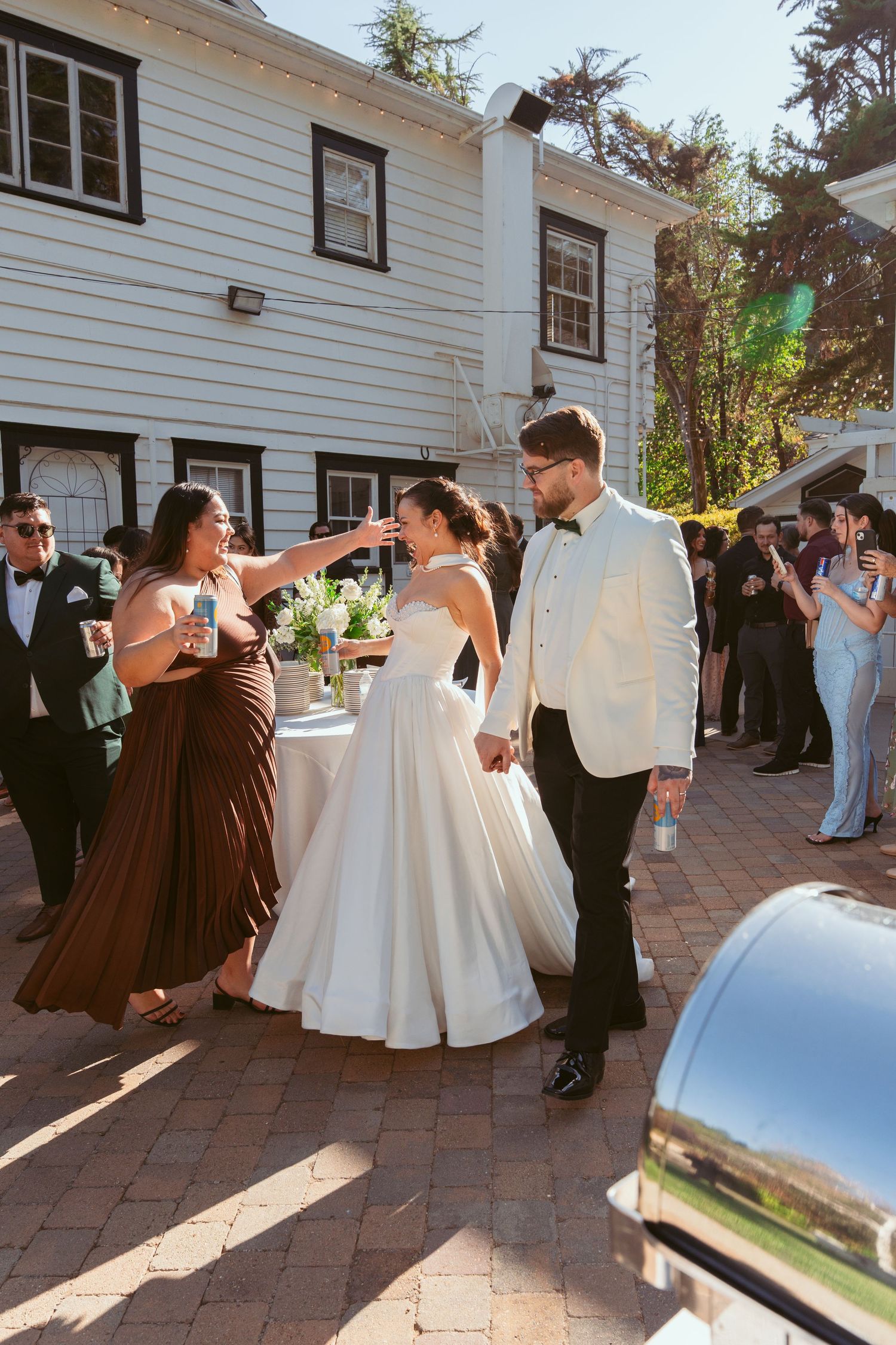 Wedding celebration on a brick patio outside a white clapboard house with formal attire.