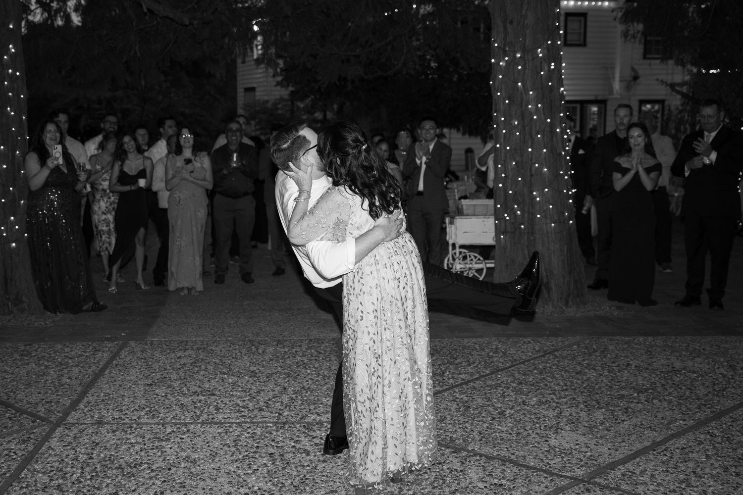 Black and white photo of couples dancing at an outdoor wedding reception with string lights.