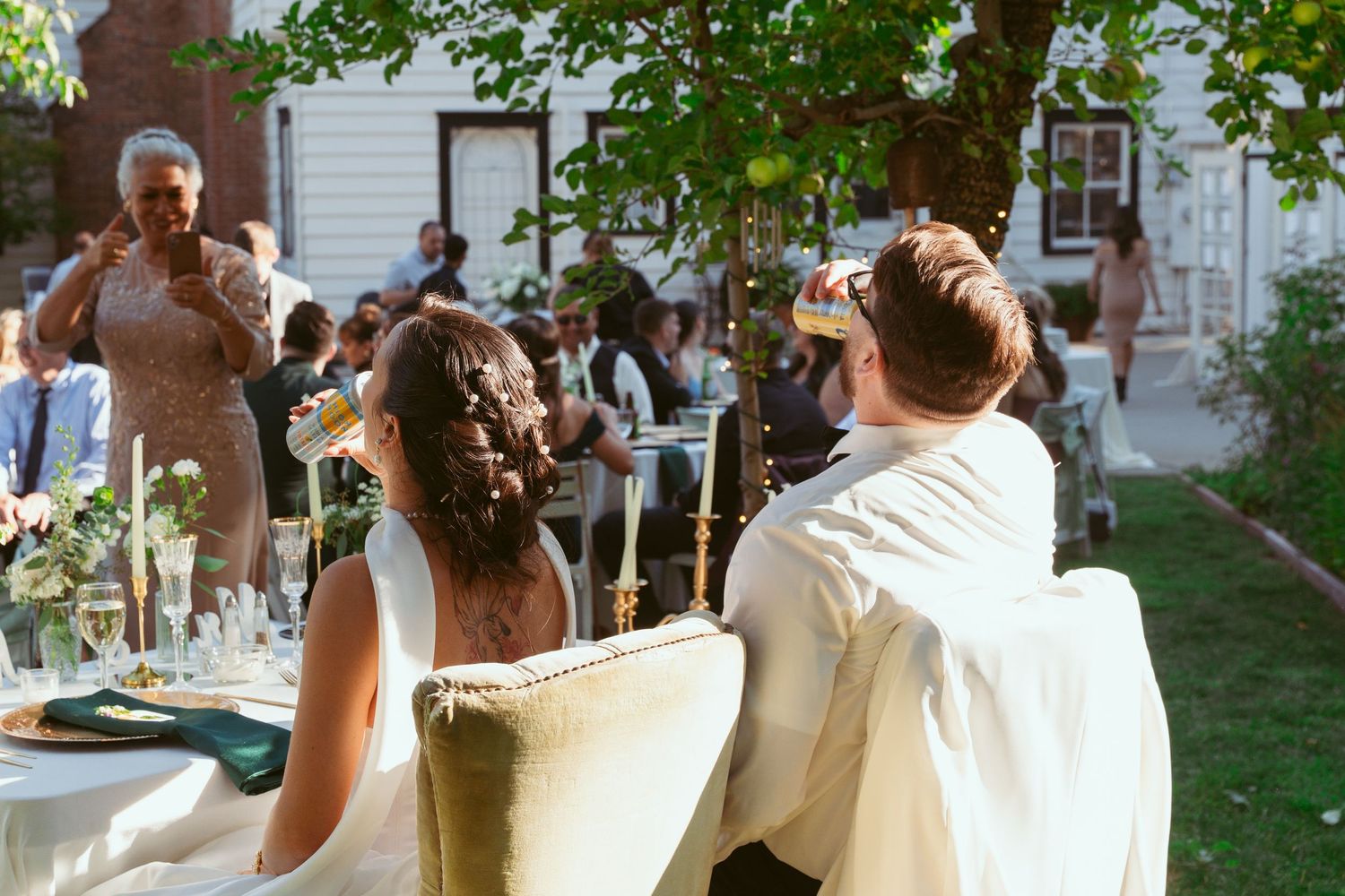 Wedding guests gathered outdoors under tree branches at a garden reception.