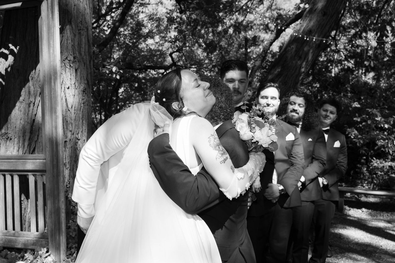 A romantic black and white wedding moment captured with guests watching in the background.