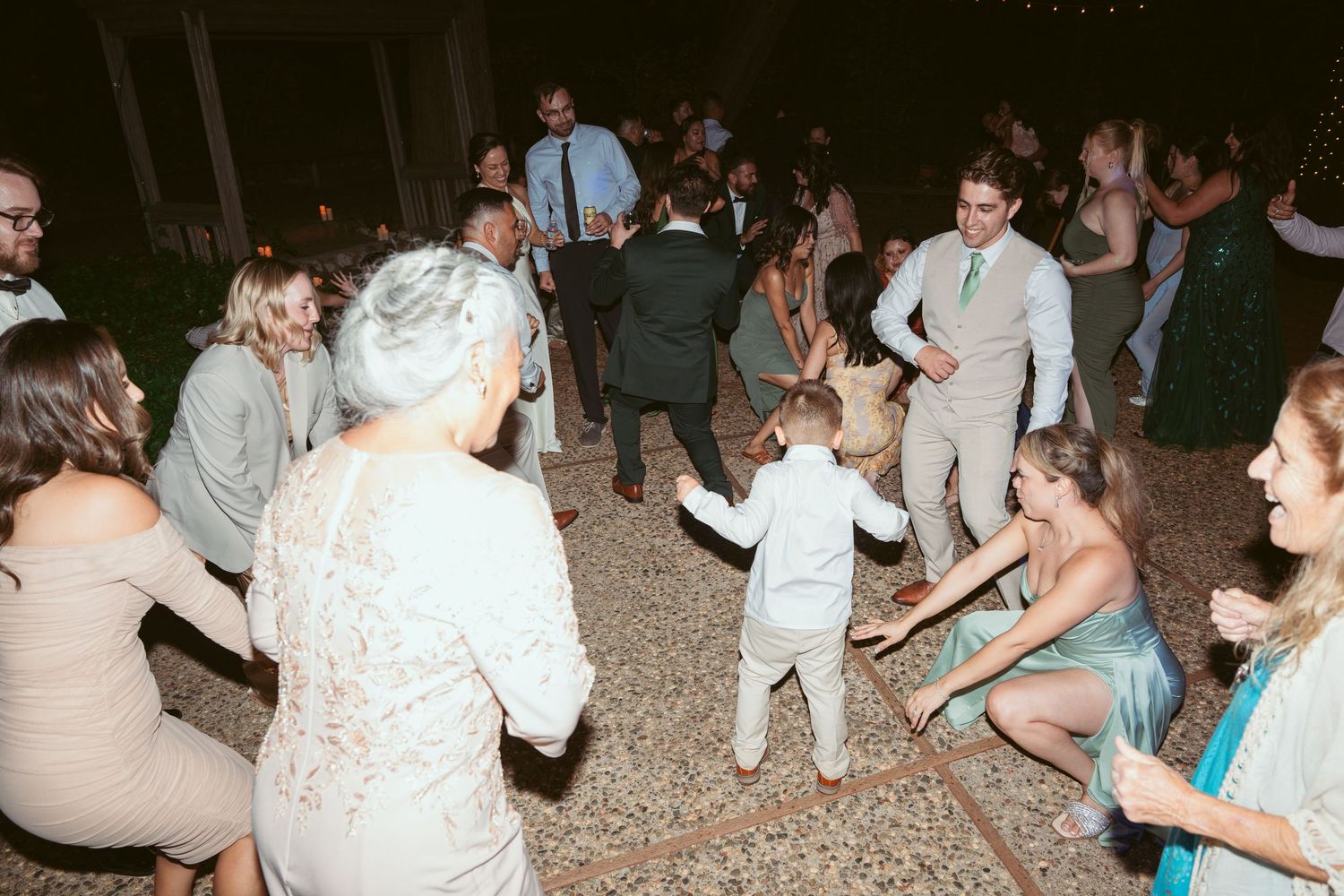 Wedding guests dance and celebrate on an outdoor patio with string lights.