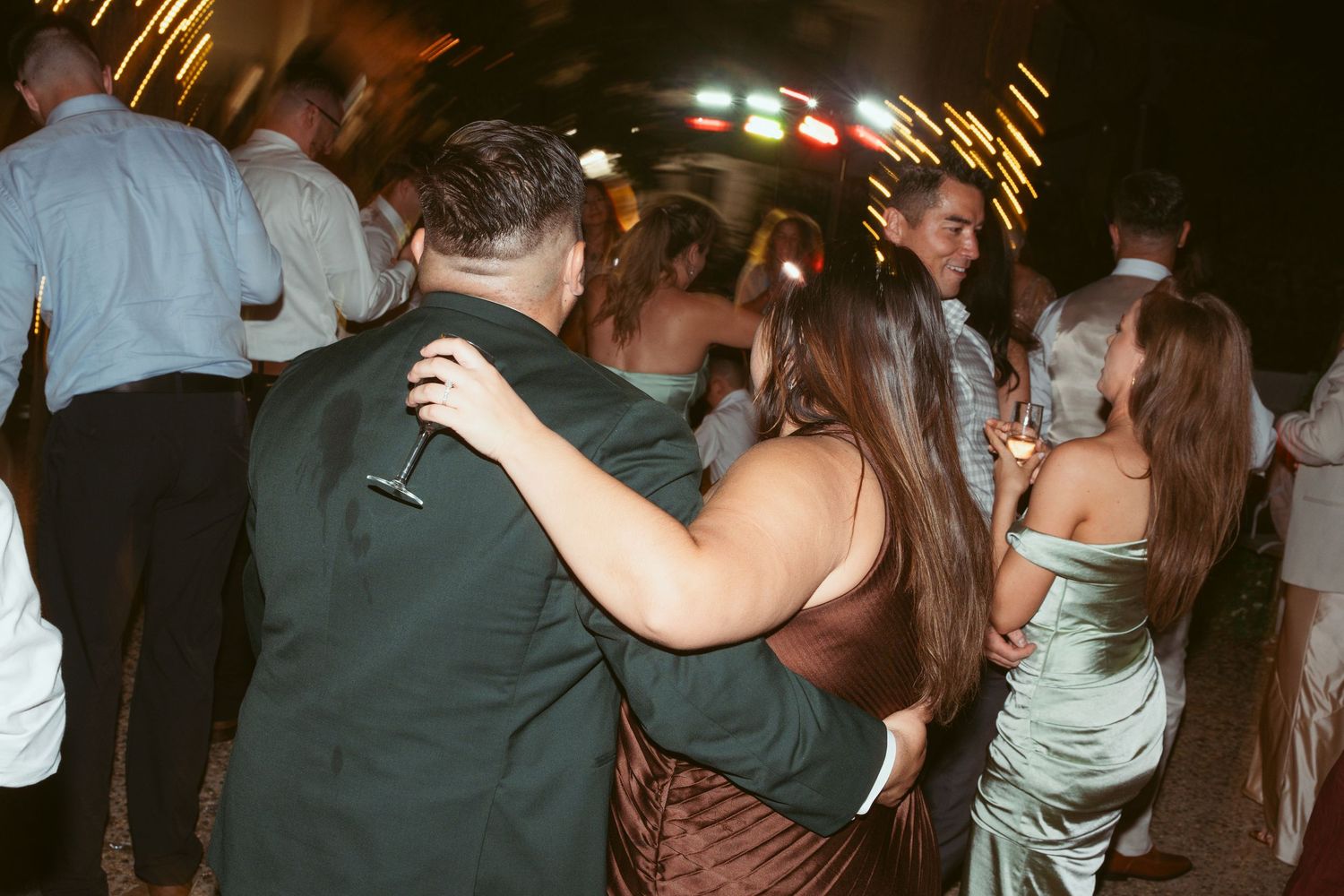 Wedding guests dancing together at a dimly lit reception with string lights overhead.