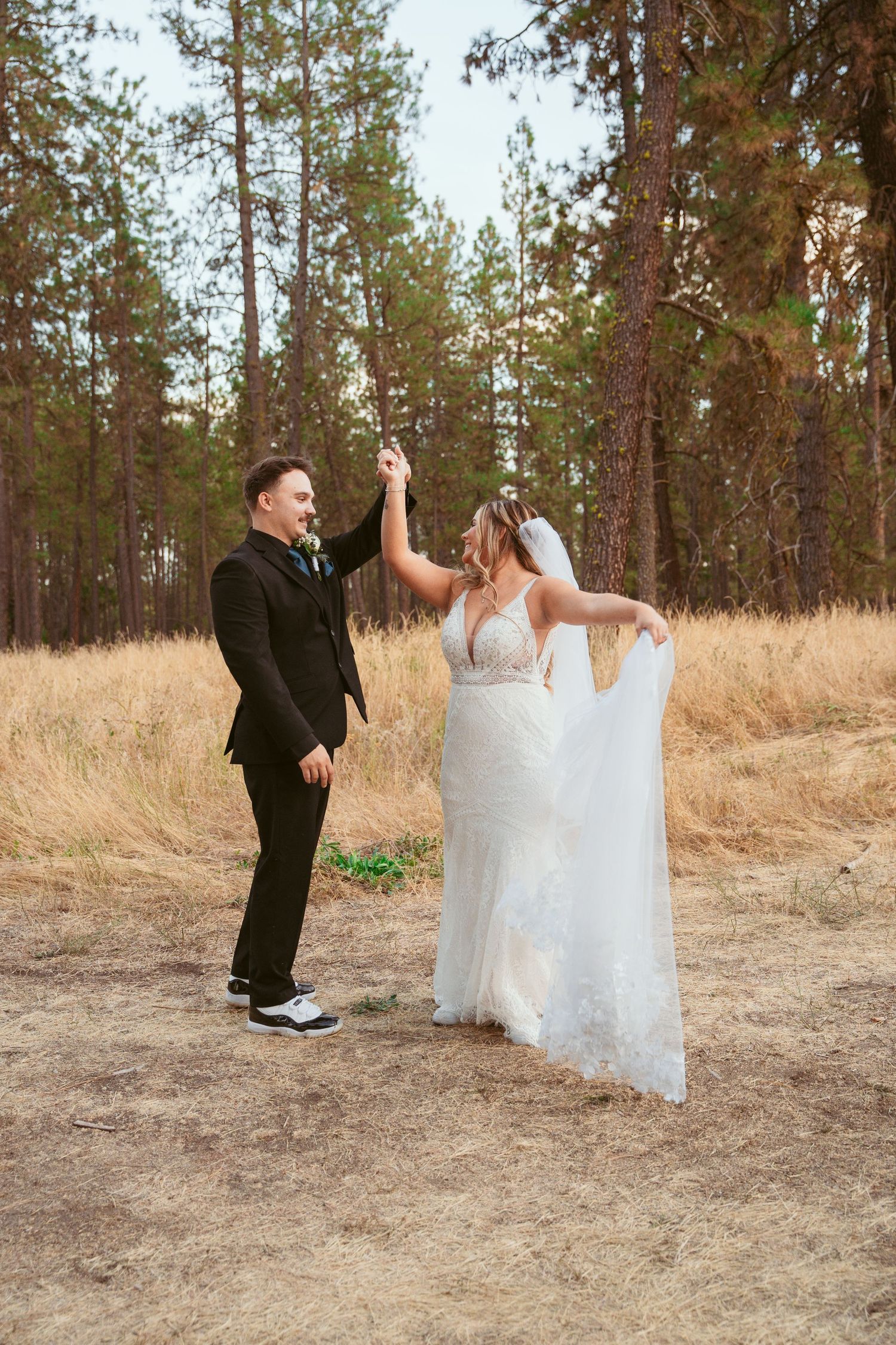 Wedding couple dances and twirls in a rustic outdoor setting with pine trees in the background.