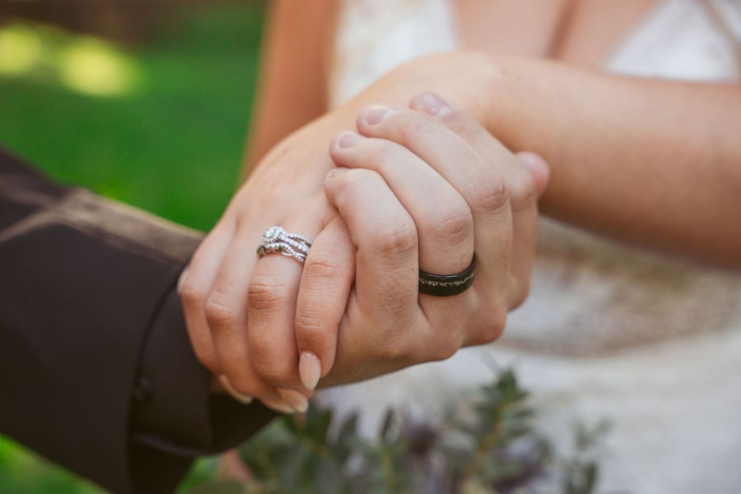 Close-up of hands showing wedding rings in natural outdoor lighting.