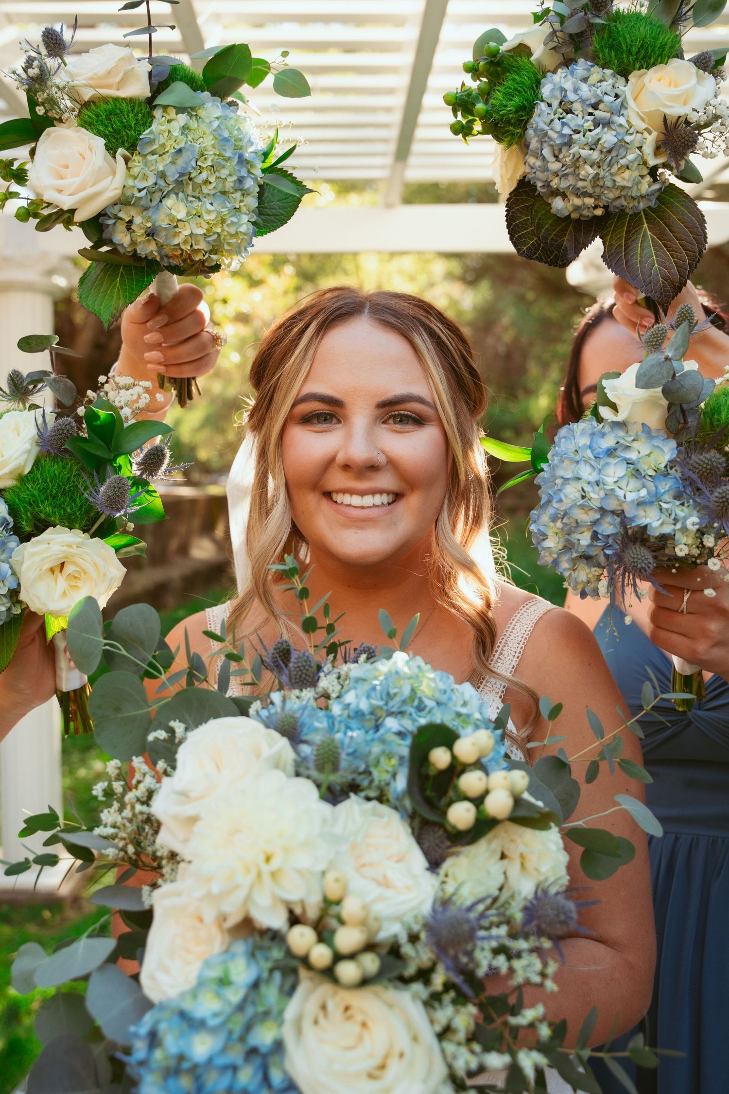 Wedding bouquets featuring blue hydrangeas and white roses held by wedding party members in navy dresses.