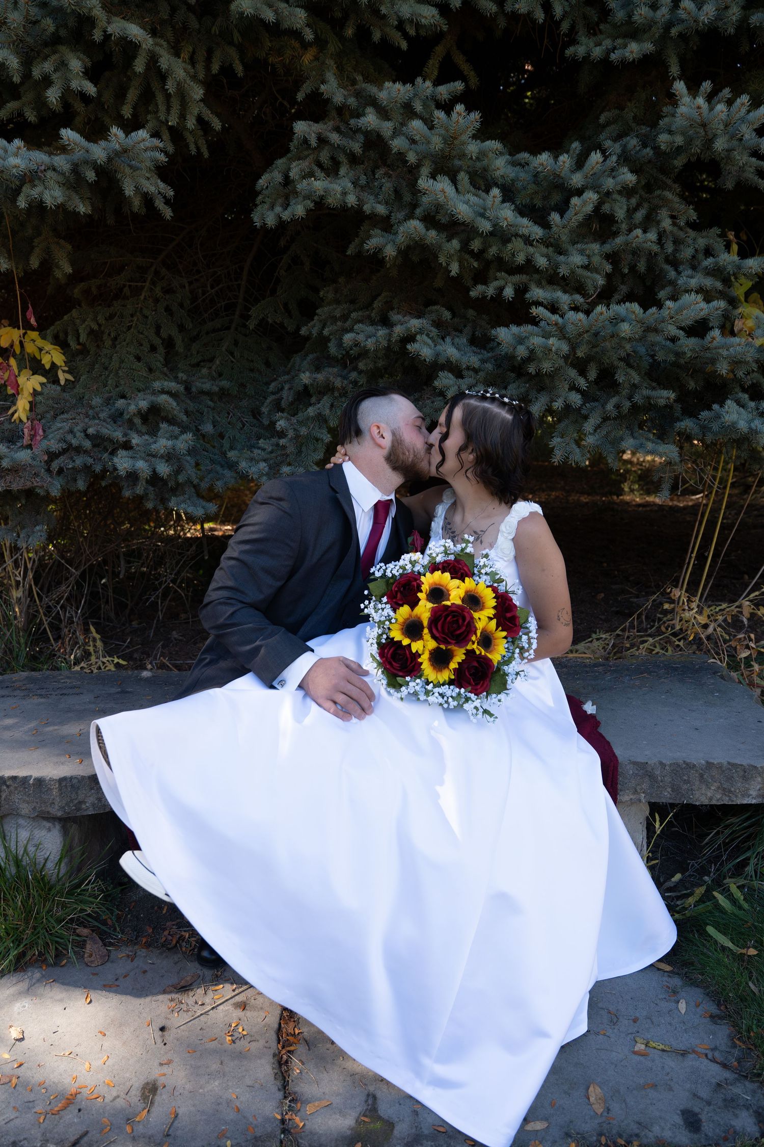 Wedding couple poses on stone bench with dramatic lighting and sunflower bouquet.