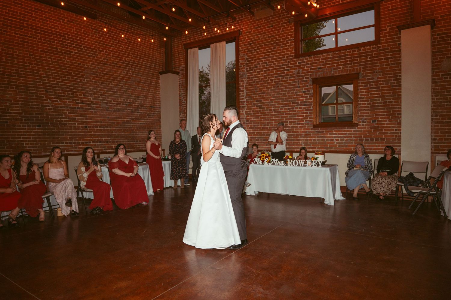 Romantic first dance moment in a warmly lit brick venue with guests looking on.