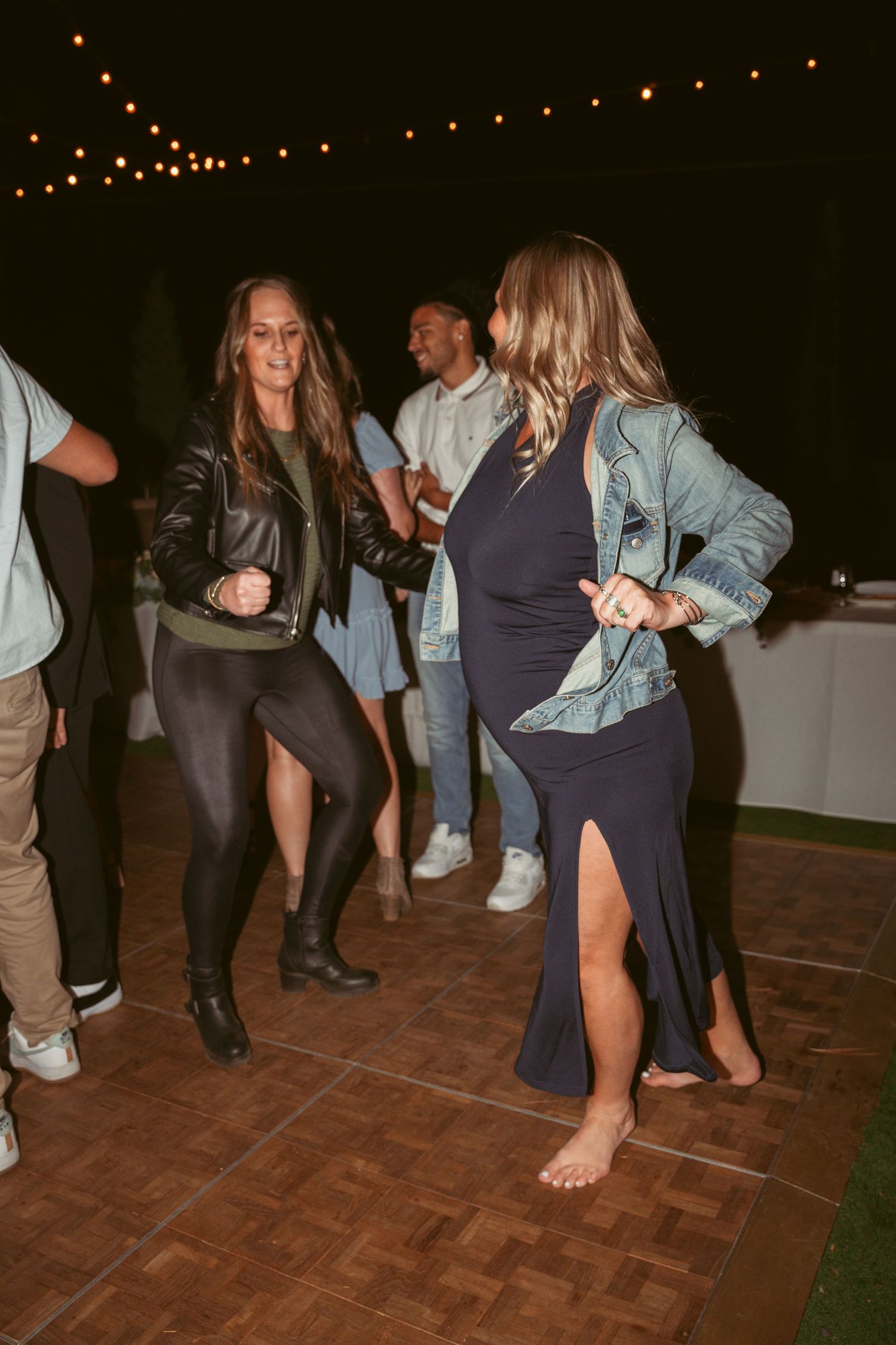 Wedding guests dancing barefoot on a wooden dance floor at night.