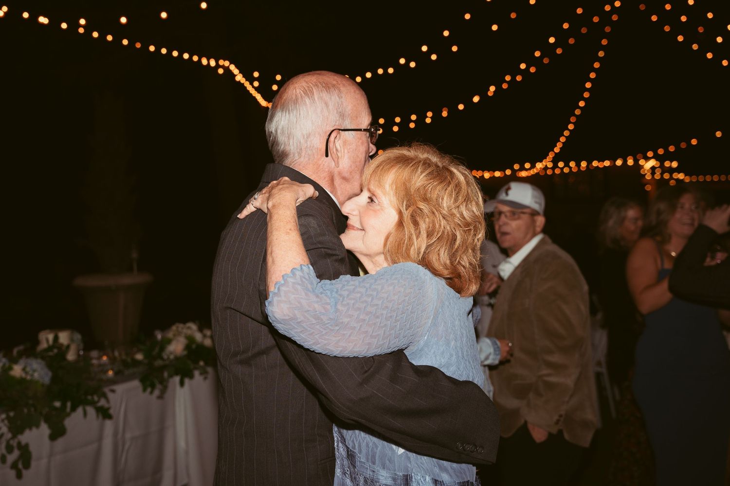 Couples dancing together beneath romantic string light decorations at outdoor wedding.