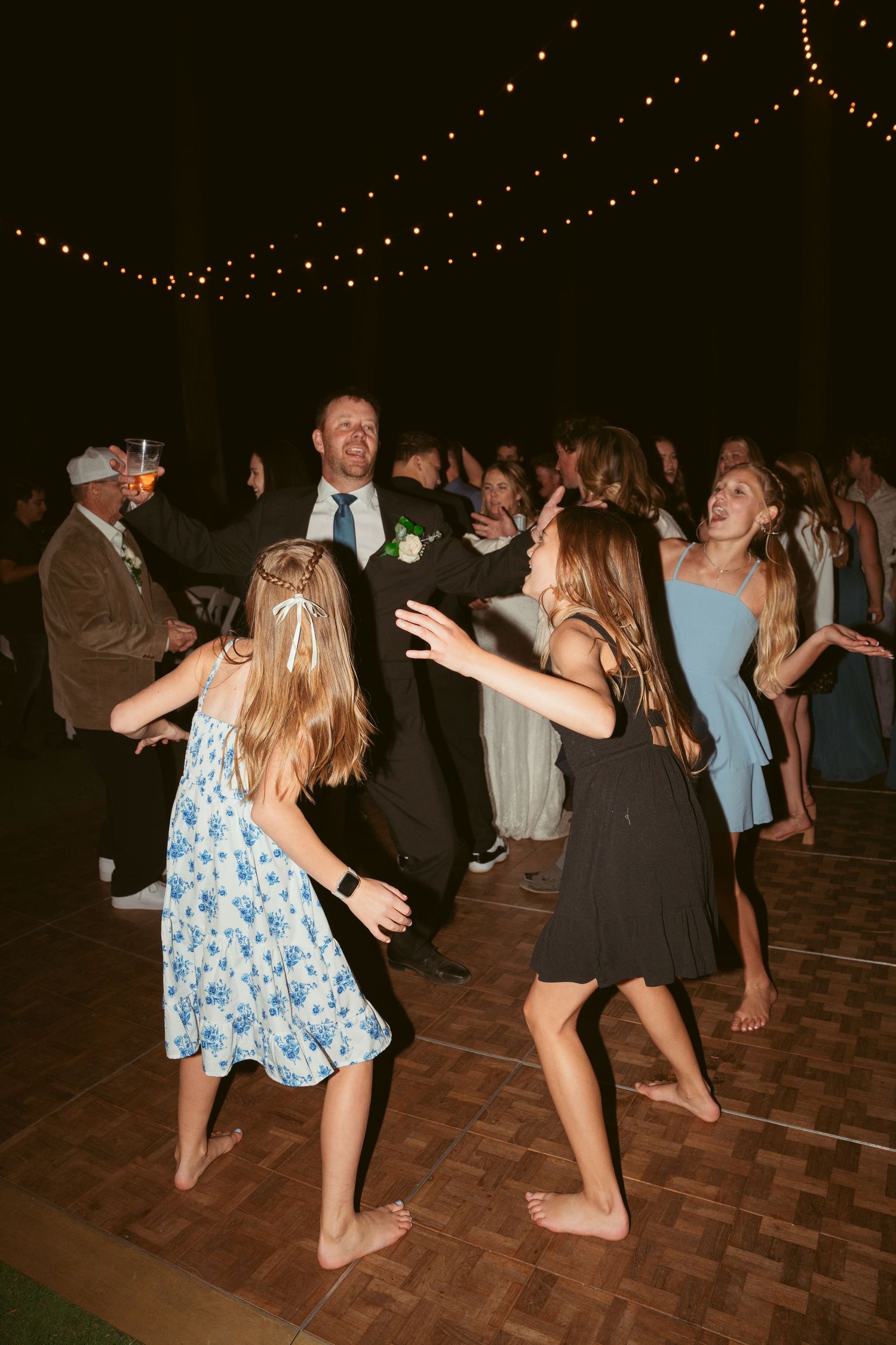 Guests dancing barefoot in summer dresses and casual wear at an evening wedding reception.