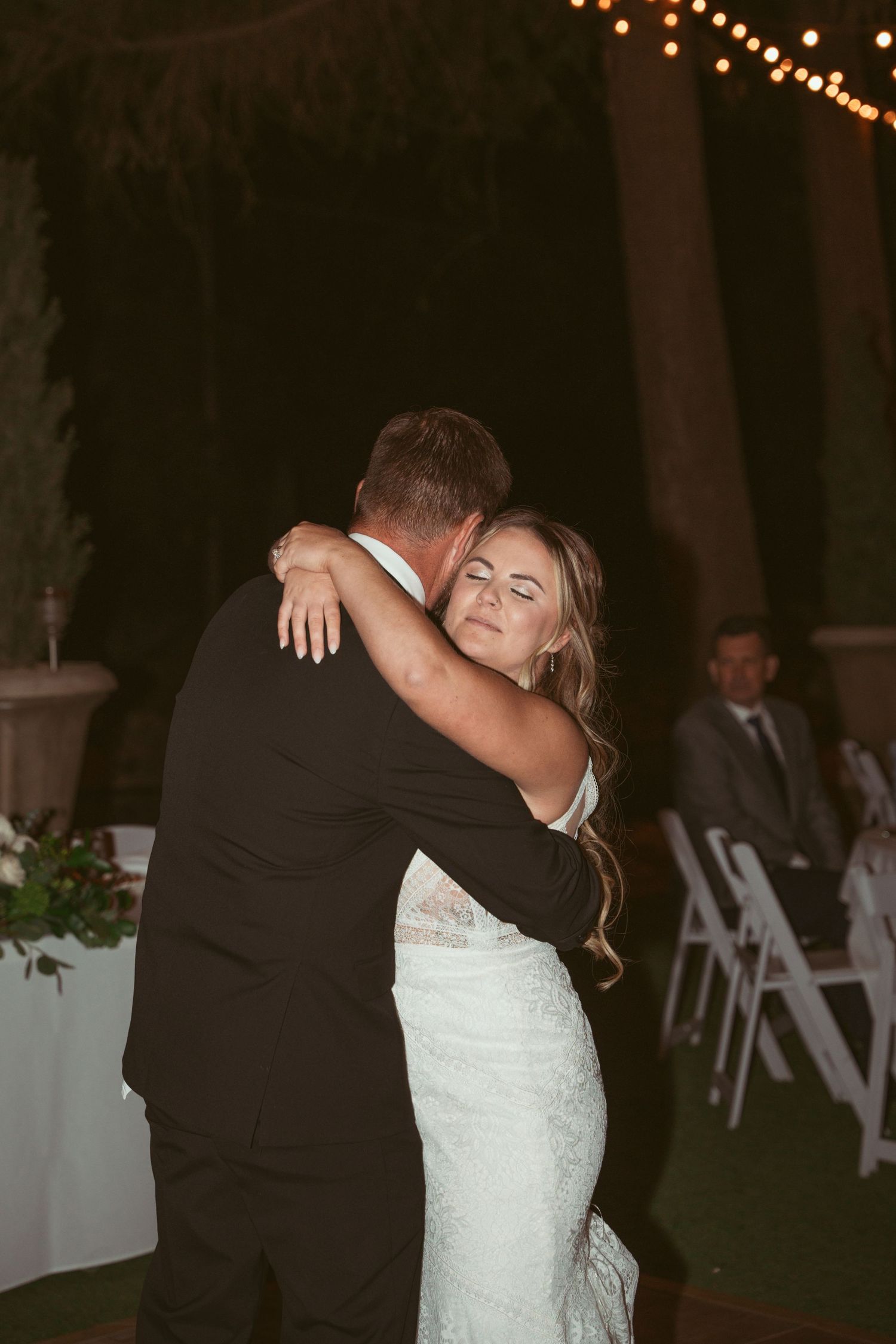 A couple shares an intimate slow dance moment at their wedding reception under string lights.